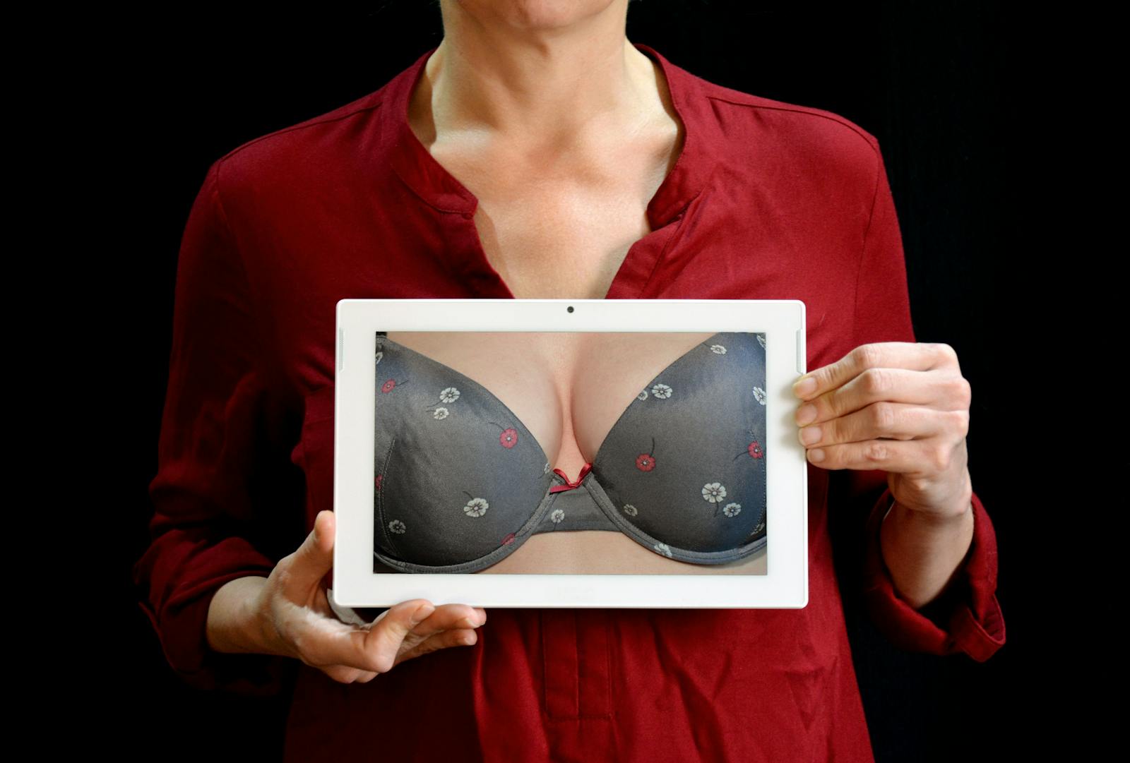 Photo by Pixabay Adult woman in red shirt holding a tablet showing a lingerie closeup, studio shot.