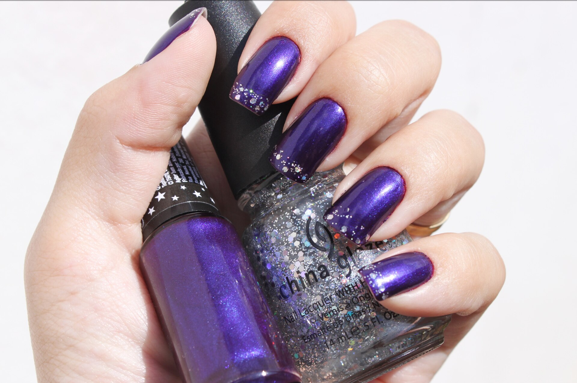 g-vernis Main aux ongles vernis violet métallisé tenant deux flacons de vernis