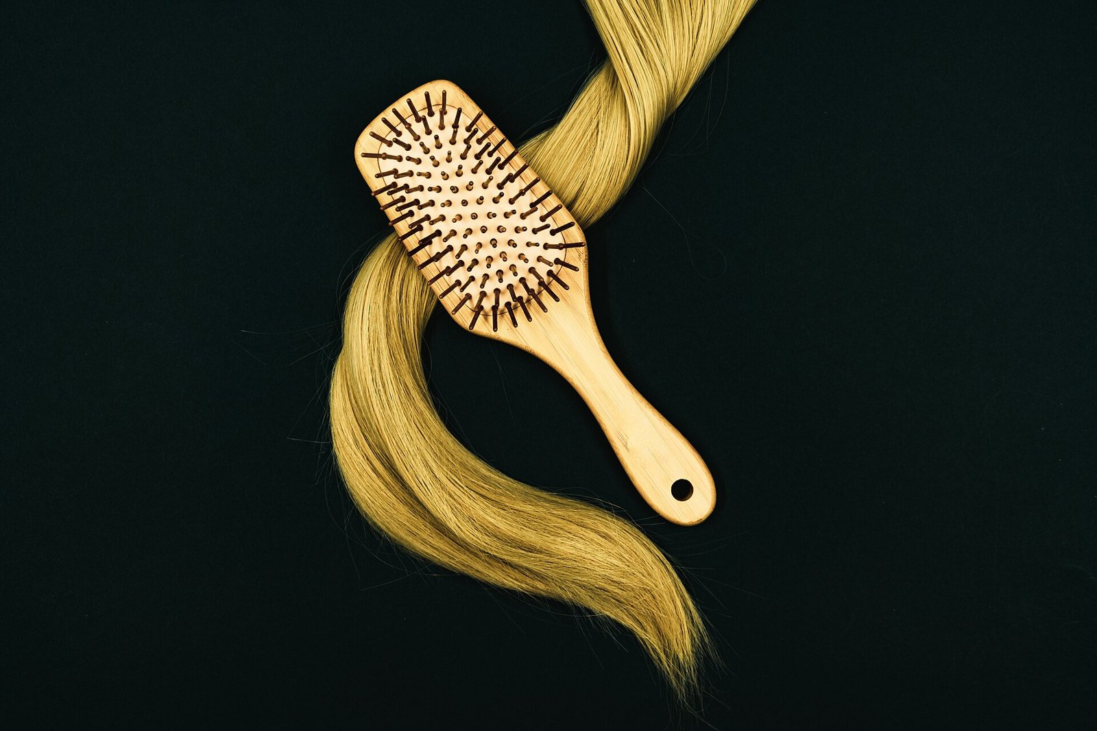 Brosse à cheveux en bois posée sur une mèche blonde, sur fond sombre