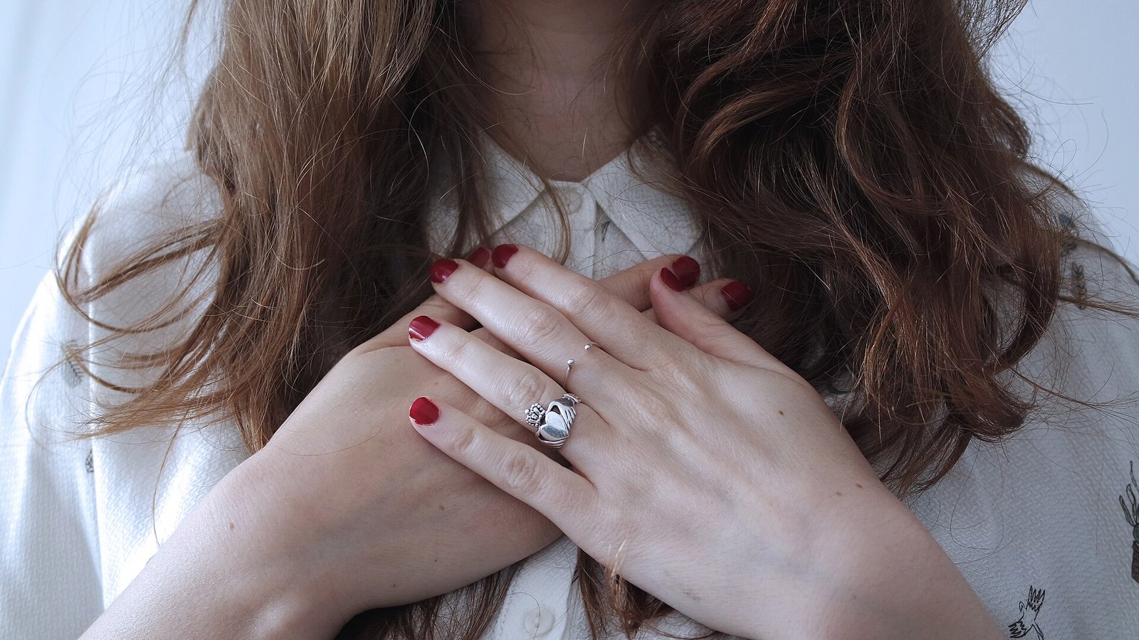 Mains croisées sur un chemisier blanc, ongles courts vernis de rouge